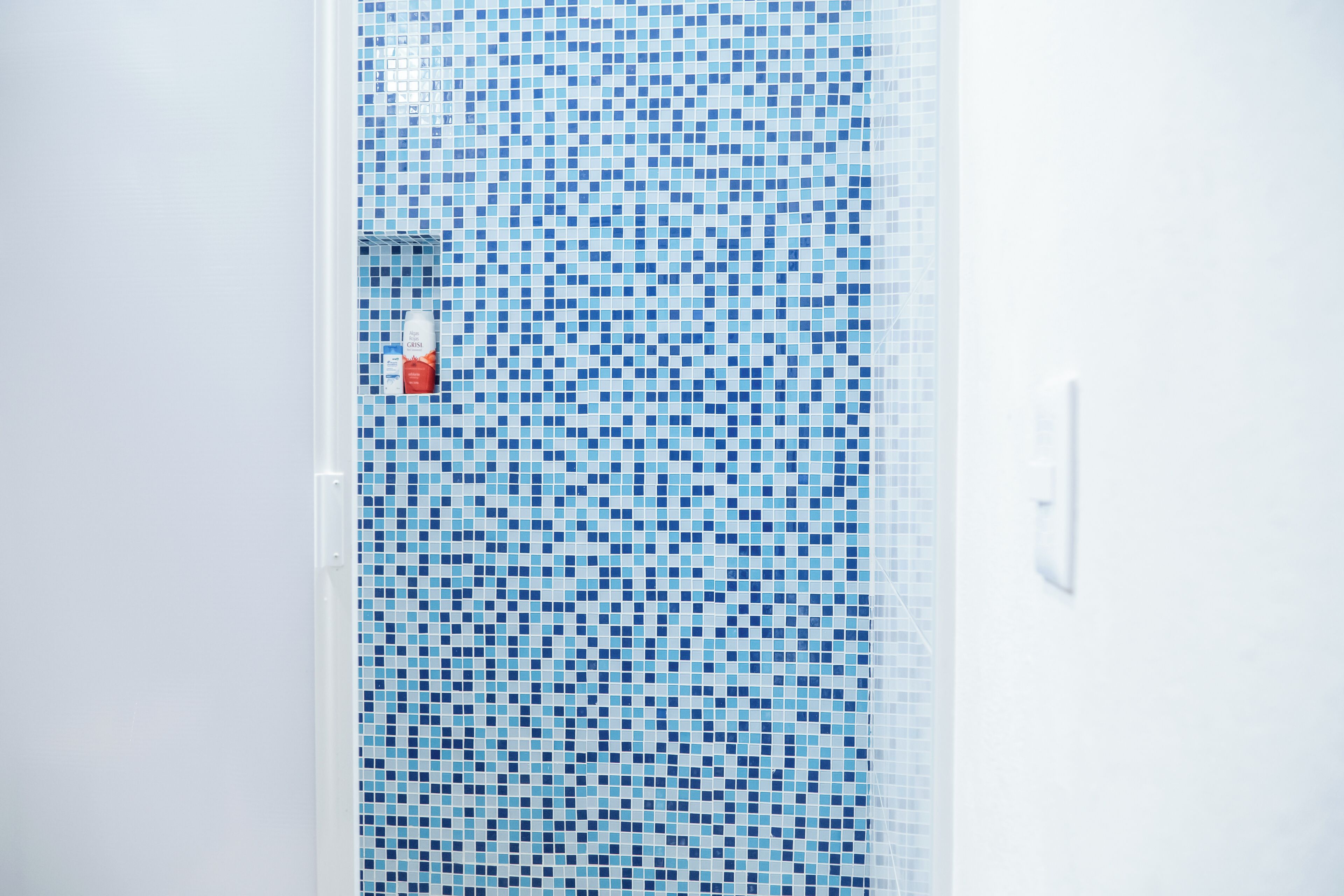 A bathroom with a blue mosaic tile wall and a white door.