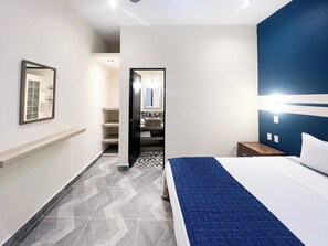 A hotel room with a bed, a nightstand, a mirror, and a bathroom visible through an open door.