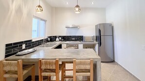 A modern kitchen with a central island, stainless steel appliances, and a dining area with wooden chairs. - Casa Coral (Sayulita)