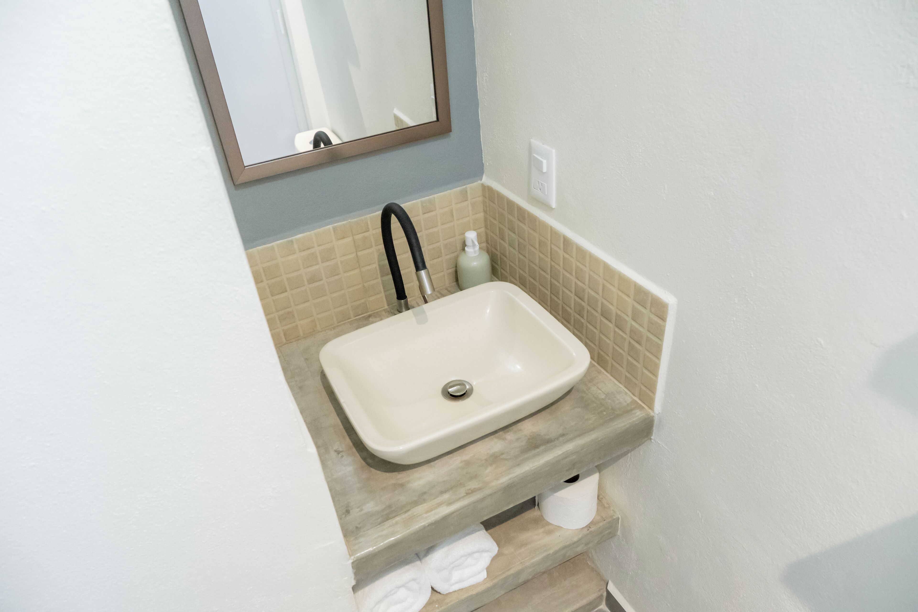 Un baño con un lavabo color beige, un espejo, un perchero y una botella de jabón para manos.