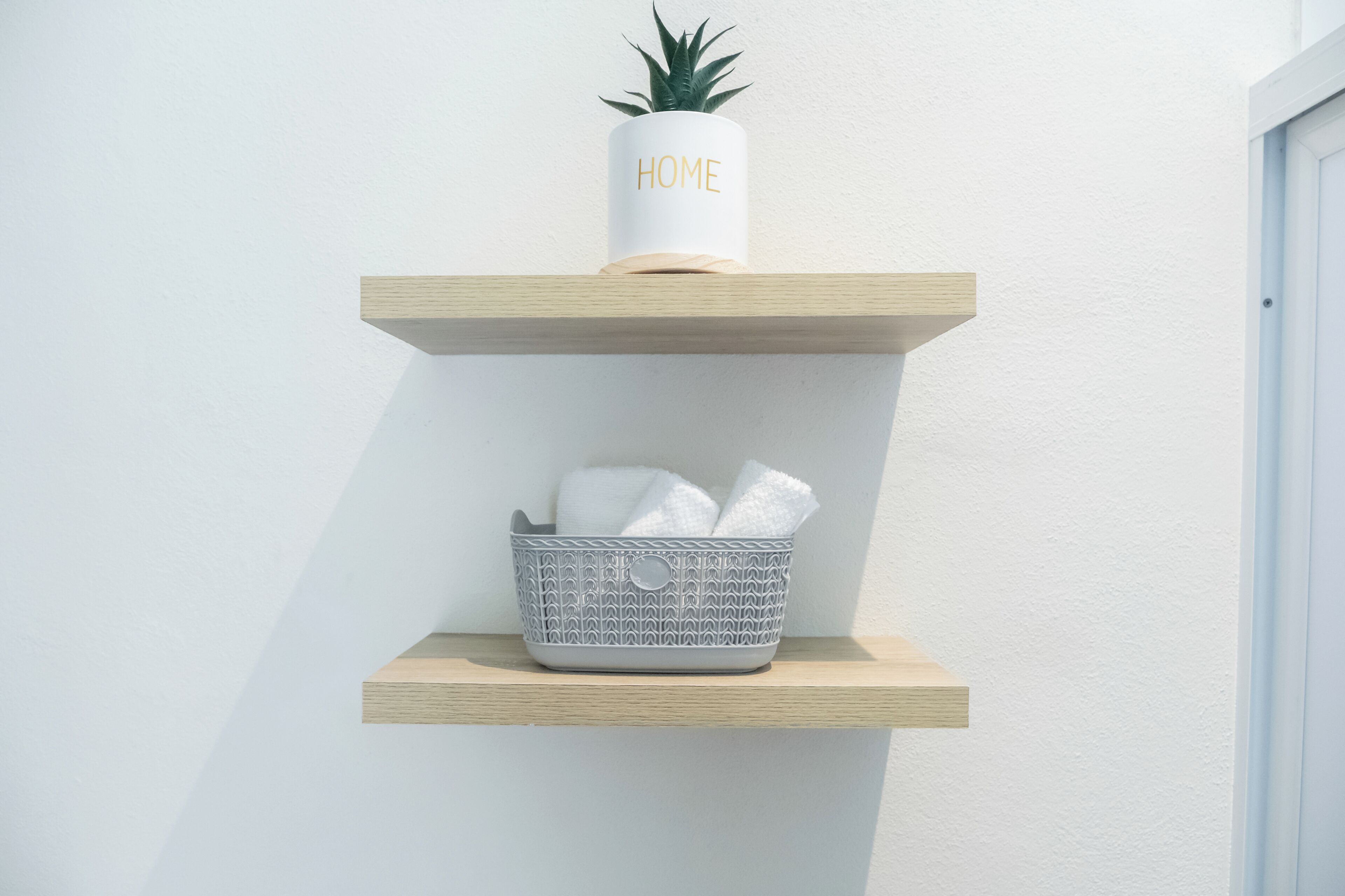 A white potted plant on a wooden shelf with a basket containing towels.