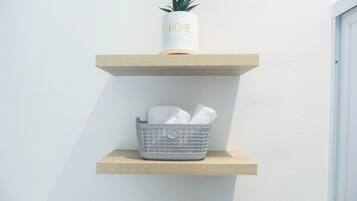 A white potted plant on a wooden shelf with a basket containing towels.