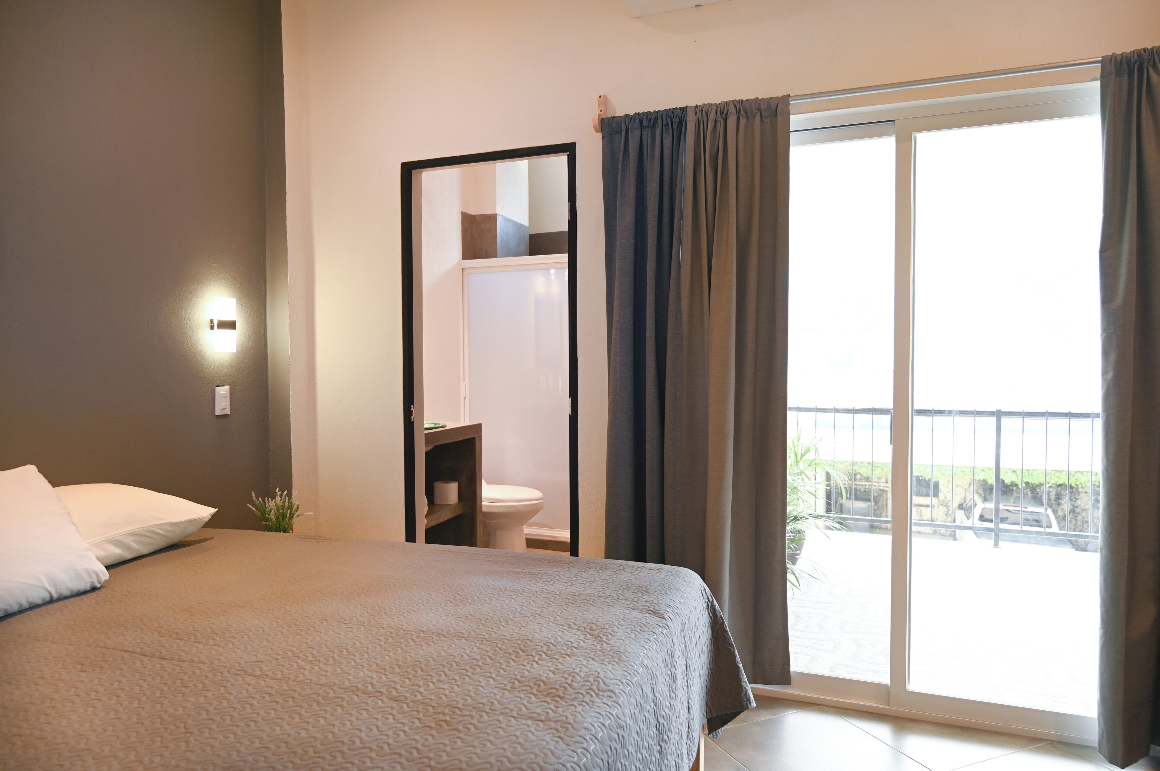 A hotel room with a bed, a bathroom, and a view of the outside.