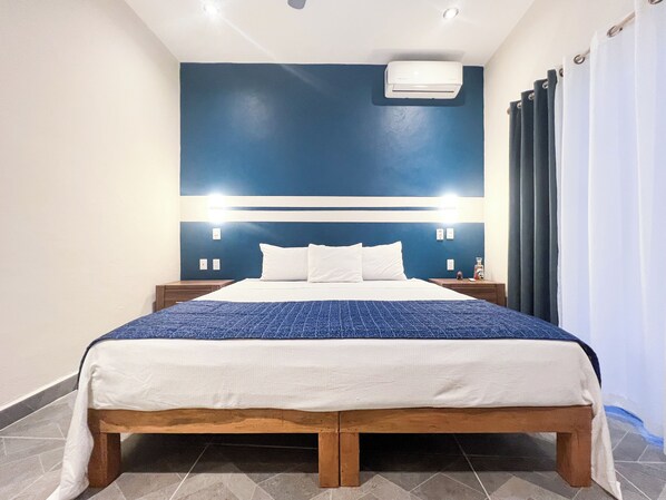 A hotel room with a bed, nightstands, an air conditioning unit, and a curtain. - Casa Coral (Sayulita)