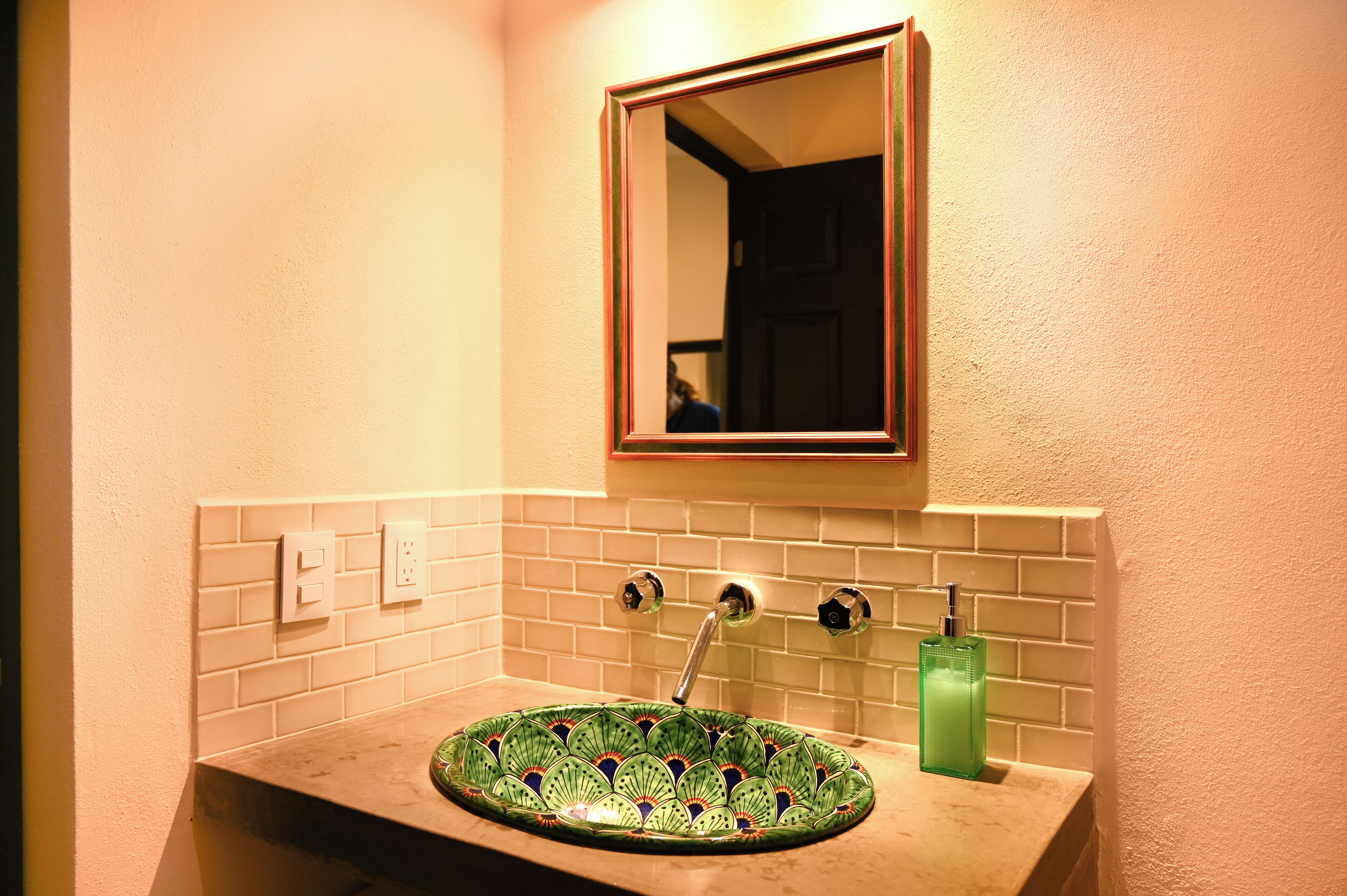 A bathroom with a green patterned sink, a mirror above it, and a green bottle on the counter.