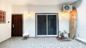A room with a patterned floor, a sliding glass door, a white chair, and a surfboard against the wall. - Casa Coral (Sayulita)