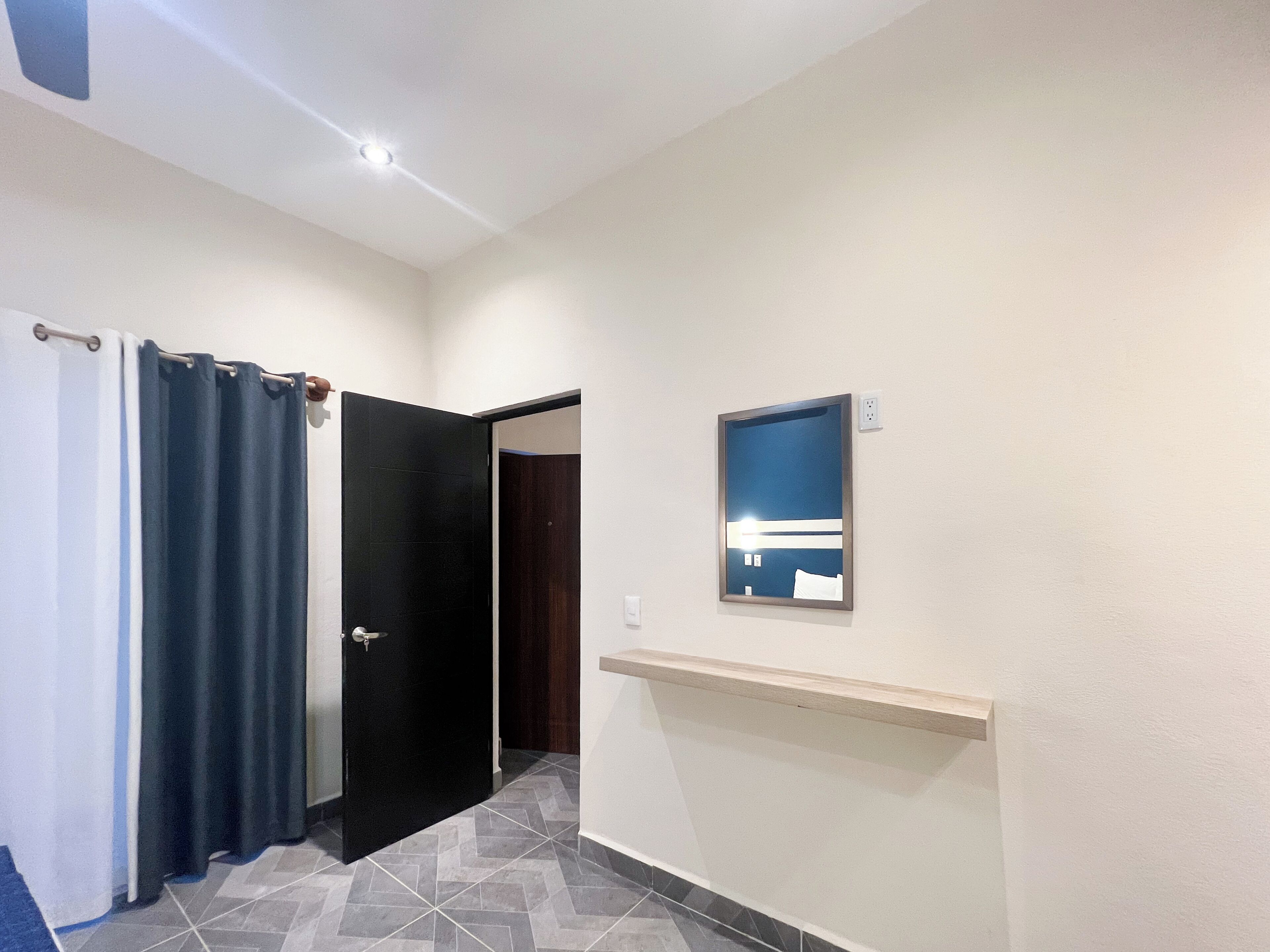 A hallway with a black door, a mirror on the wall, and a shower curtain.