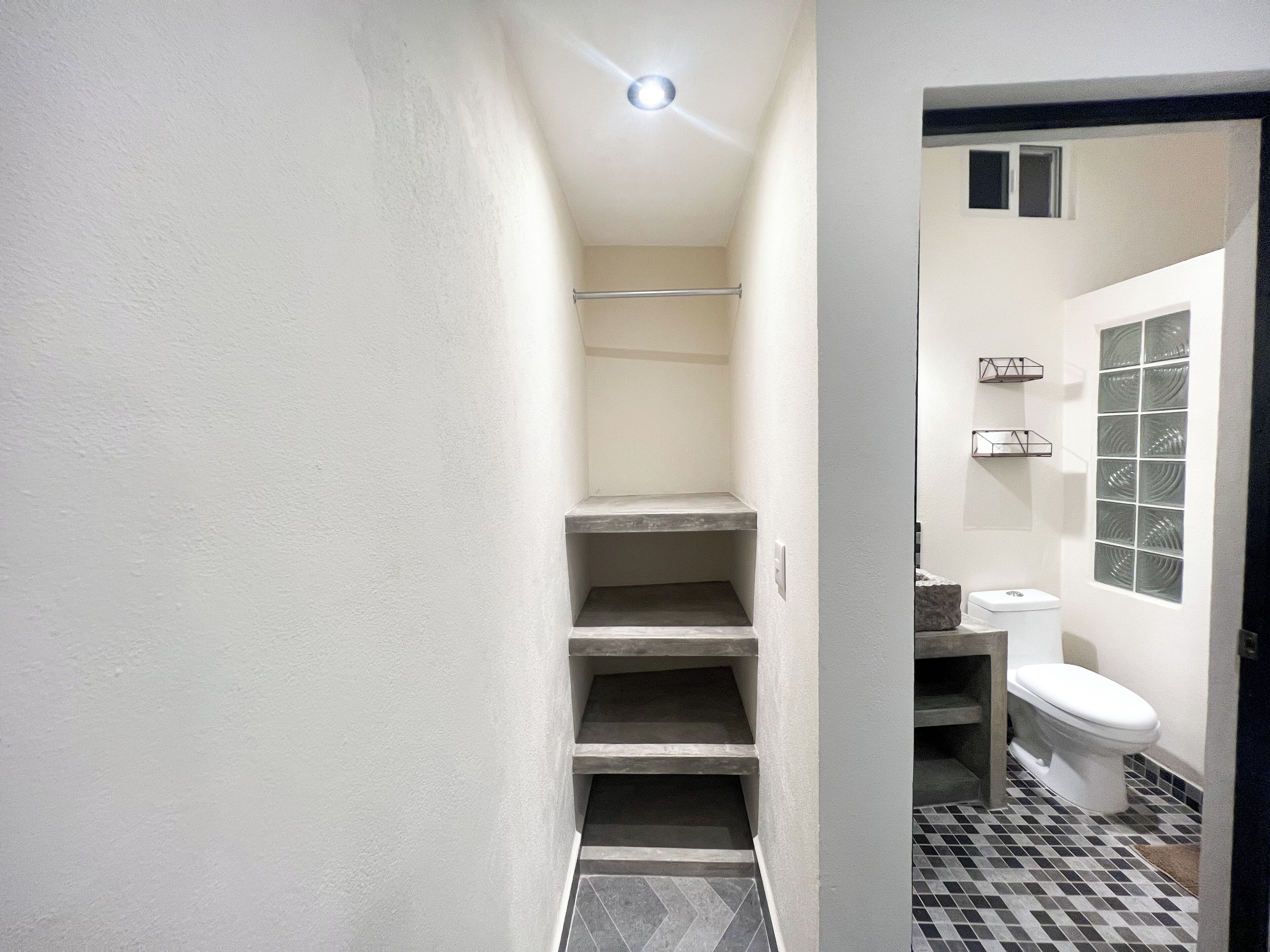 A narrow hallway leading to a bathroom with a toilet, a small window, and a tiled floor.