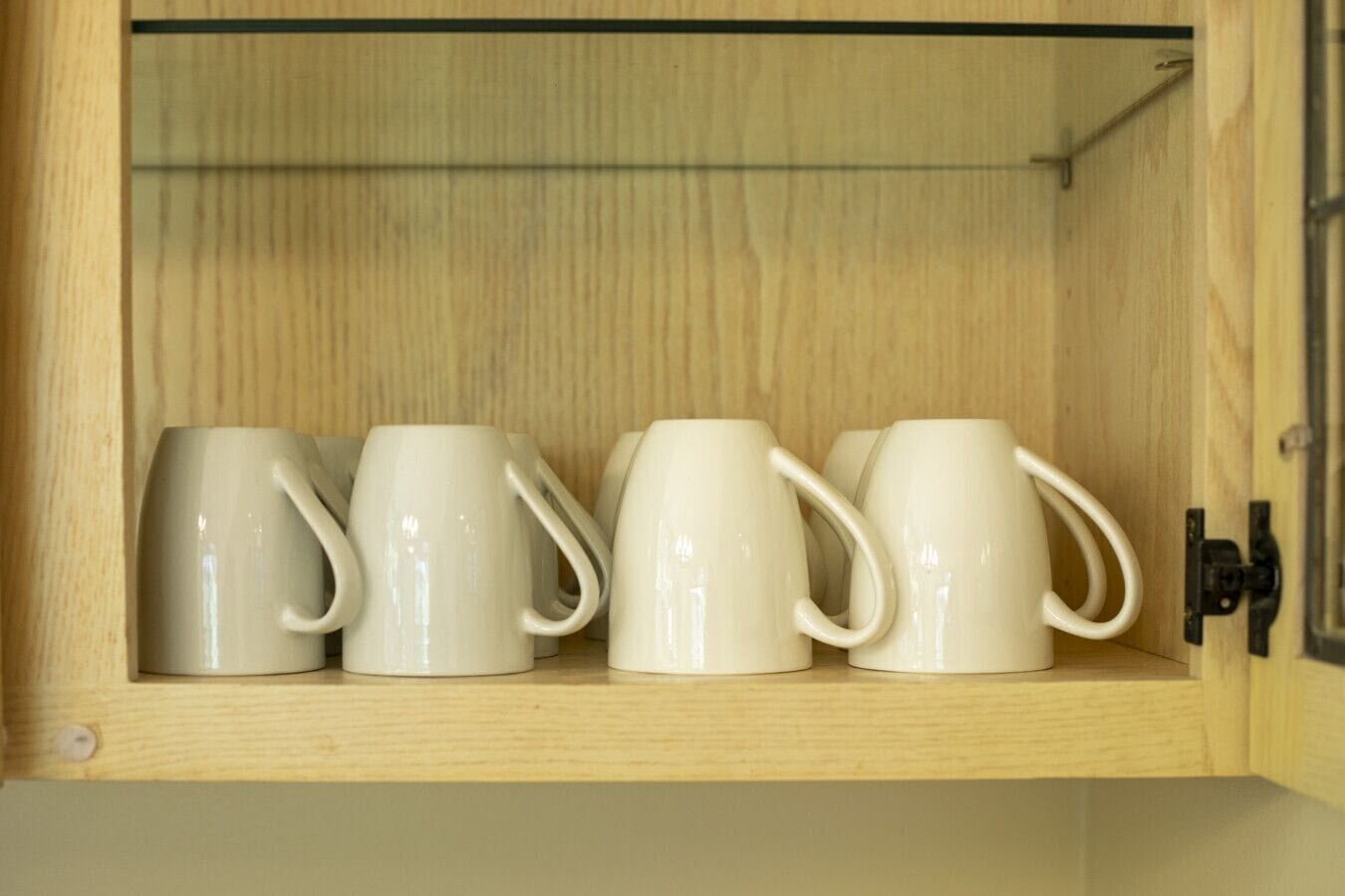 A wooden cabinet with a glass door containing four white ceramic mugs.