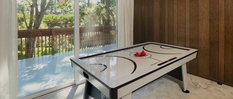 A room with a foosball table, large windows, and a view of a wooden deck and trees.