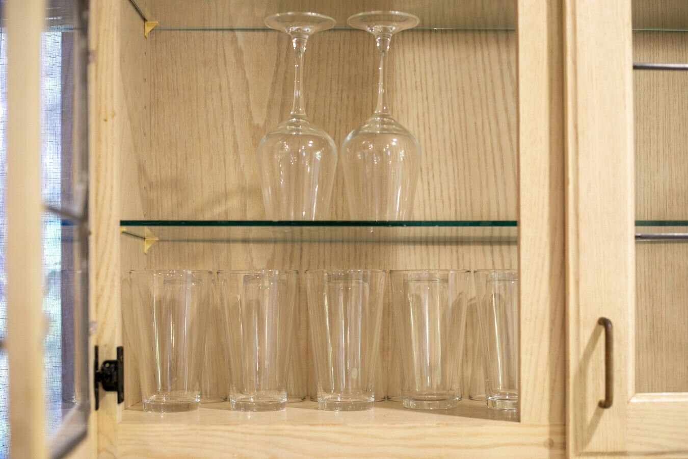 Un mueble de madera con dos estantes; la parte superior contiene dos copas de vino y la inferior, seis vasos de cristal.