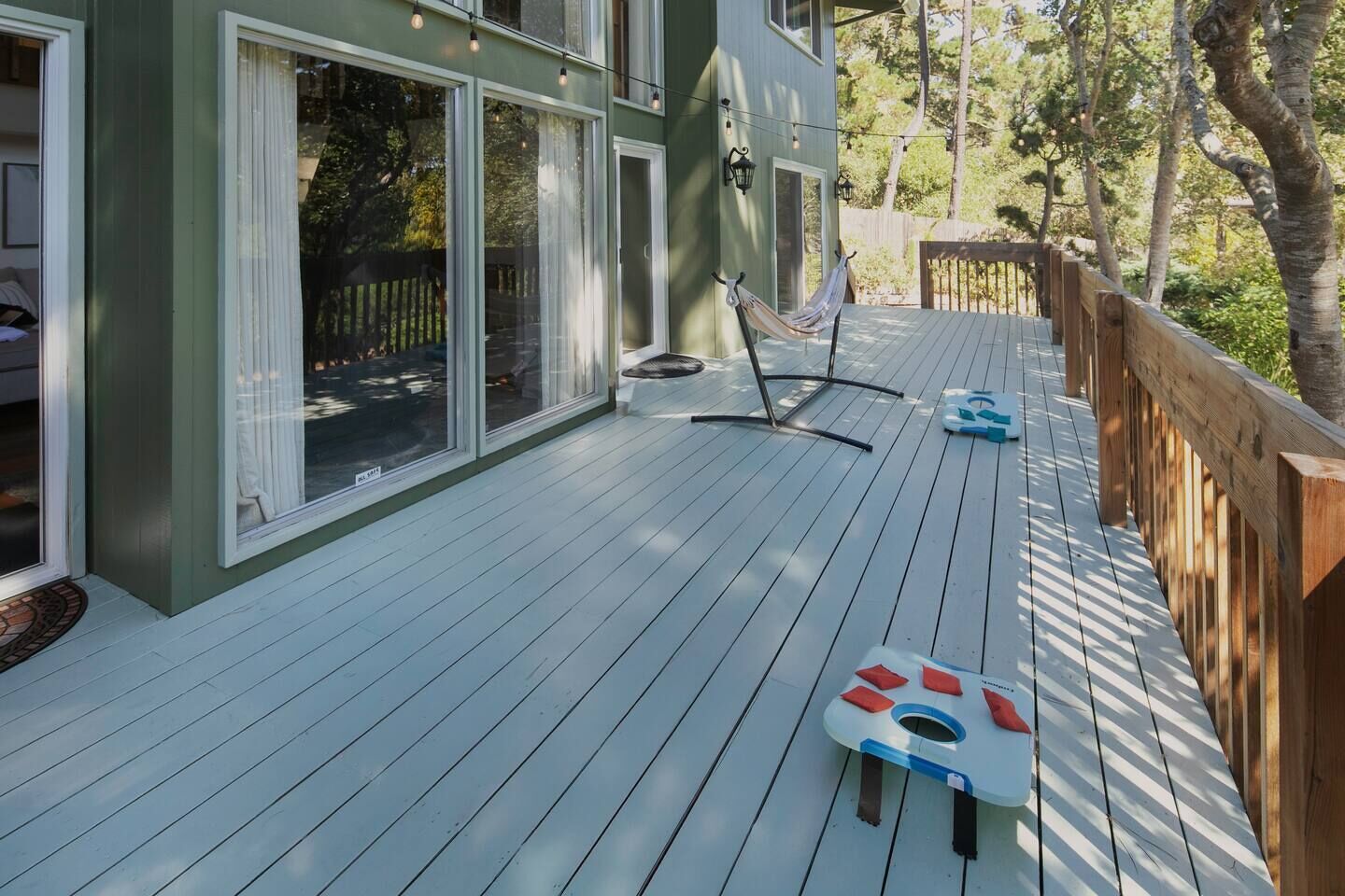 Een houten terras met een hangmat en een paddleboard, omringd door een houten hek en bomen.