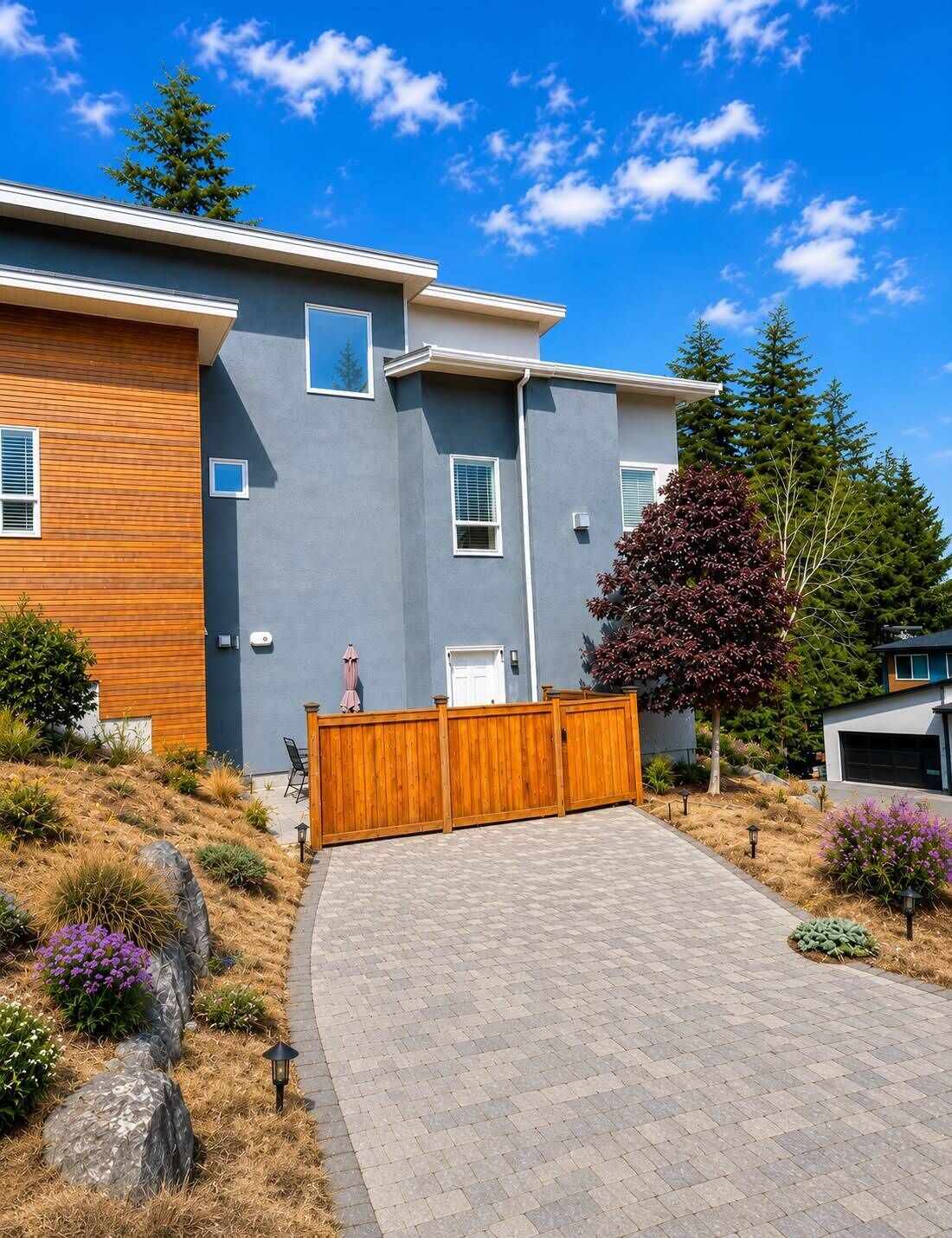 A modern two-story house with a grey exterior, a wooden fence, and a paved driveway.