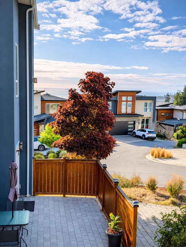 Una zona residencial con casas modernas, una cerca de madera, un camino de entrada pavimentado y vista al mar.