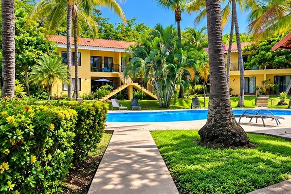 A yellow building with a swimming pool, surrounded by palm trees and greenery.