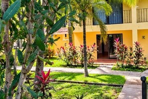 A yellow building with a balcony, surrounded by greenery and plants.