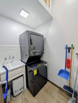 A compact bathroom with a sink, a black washing machine, a mop, and a broom.