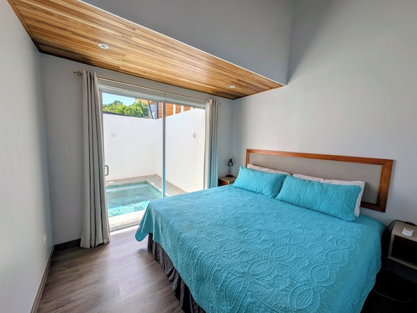 A bedroom with a large bed, a wooden ceiling, and a sliding glass door leading to an outdoor area.