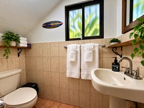 A bathroom with a toilet, sink, and window. There are towels hanging on a rack and a plant on a shelf.