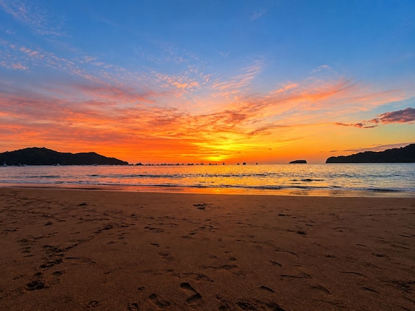 A beach with footprints in the sand and a sunset in the background.