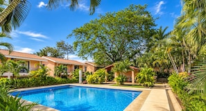 A swimming pool surrounded by lush greenery and a building with a tiled roof.