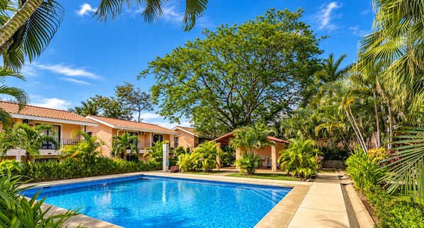 A swimming pool surrounded by lush greenery and a building with a tiled roof.