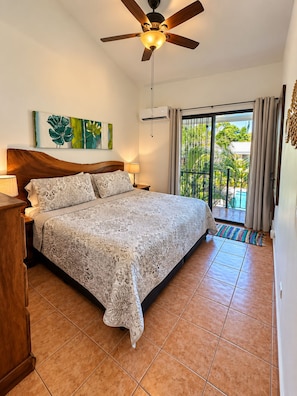 A bedroom with a bed, a ceiling fan, a window with curtains, and a view of greenery outside.