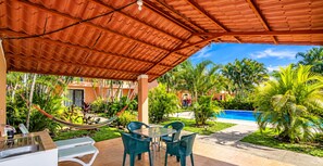 A covered outdoor area with a pool, green chairs, and a hammock.