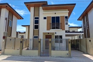 A modern two-story residential building with a gated entrance, a balcony on the upper floor, and a flat roof. - Solar-Powered Vacation Home Near Airport & Beaches (Dauis)