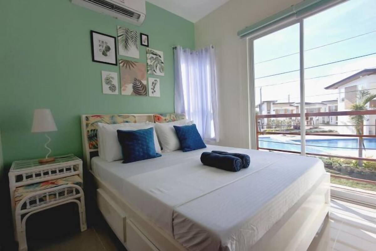 A bedroom with a bed, a nightstand, a lamp, and a view of a swimming pool.