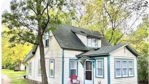 A two-story house with a porch, a red chair, and a potted plant.