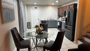 A modern kitchen with a dining area, featuring a glass table, dark chairs, and stainless steel appliances. - Peaceful Family Retreat – Minutes to AT&T & Rangers Stadiums, Six Flags & More! (Arlington)