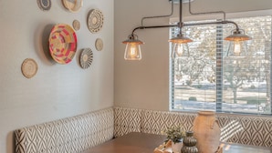 A dining area with a wooden table, patterned bench, hanging light fixture, and decorative plates on the wall.
