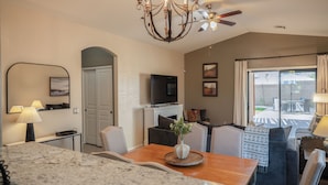 A modern living room with a wooden dining table, a chandelier, and a television on a stand.
