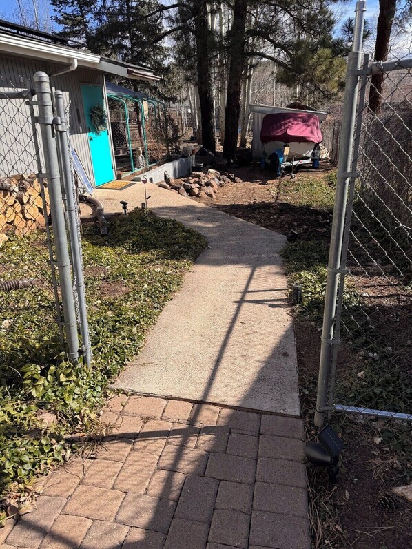 A paved pathway leading to a building with a blue door, surrounded by trees and a fenced area.