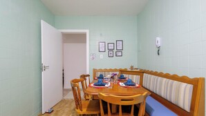 Ein Essbereich mit einem Holztisch, gedeckt für vier Personen, einer Bank mit gestreifter Sitzauflage und einer Wand mit Kacheln und gerahmten Bildern.