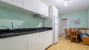 Cocina con gabinetes blancos, encimera negra y salpicadero de azulejos. Cuenta con una zona de comedor con mesa y sillas.