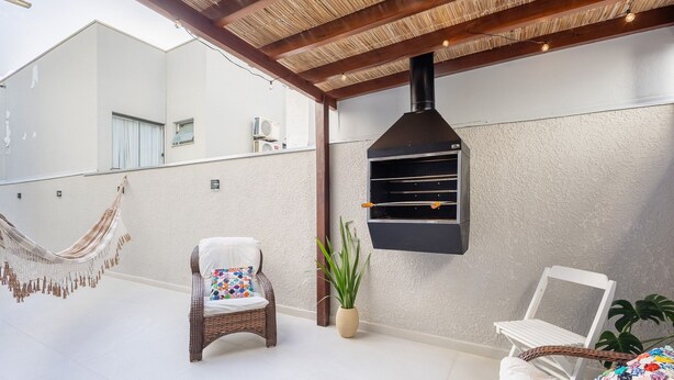 Un patio techado con una parrilla, sillas de mimbre y una hamaca.