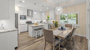 A modern kitchen with white cabinetry, a central island, and a dining area with a wooden table and chairs. - Datura Dreams (Sarasota)
