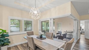 A dining area with a wooden table, cushioned chairs, and a chandelier. - Datura Dreams (Sarasota)