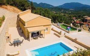 A villa with a swimming pool, outdoor seating, and a view of the surrounding landscape.