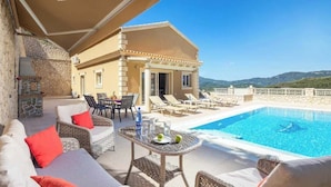 Un espace aménagé au bord de la piscine, avec des meubles en osier, une table avec des boissons et une vue sur la piscine et les montagnes.