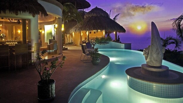 Un resort con piscina, construcciones de techo de paja y vistas al atardecer.