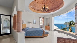 Un dormitorio con una cama grande, un balcón con vista al océano y un techo circular de ladrillo.