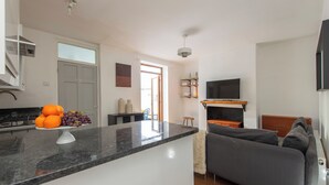 Een moderne keuken met een marmeren aanrecht, een eethoek met tafel en stoelen, een grijze bank en een aan de muur bevestigde televisie.