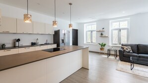 Una cocina moderna con una isla central, luces colgantes y un comedor con sofá y mesa.