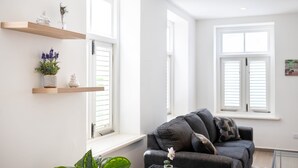 Una sala de estar moderna con un sofá gris, paredes blancas y estanterías de madera con plantas.