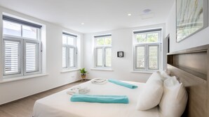 Una habitación de hotel moderna con una cama grande, ropa de cama blanca y varias ventanas.