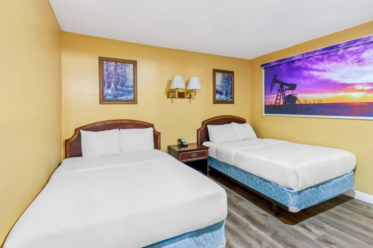 A hotel room with two beds, a nightstand, wall-mounted lamps, and a painting of an oil rig.