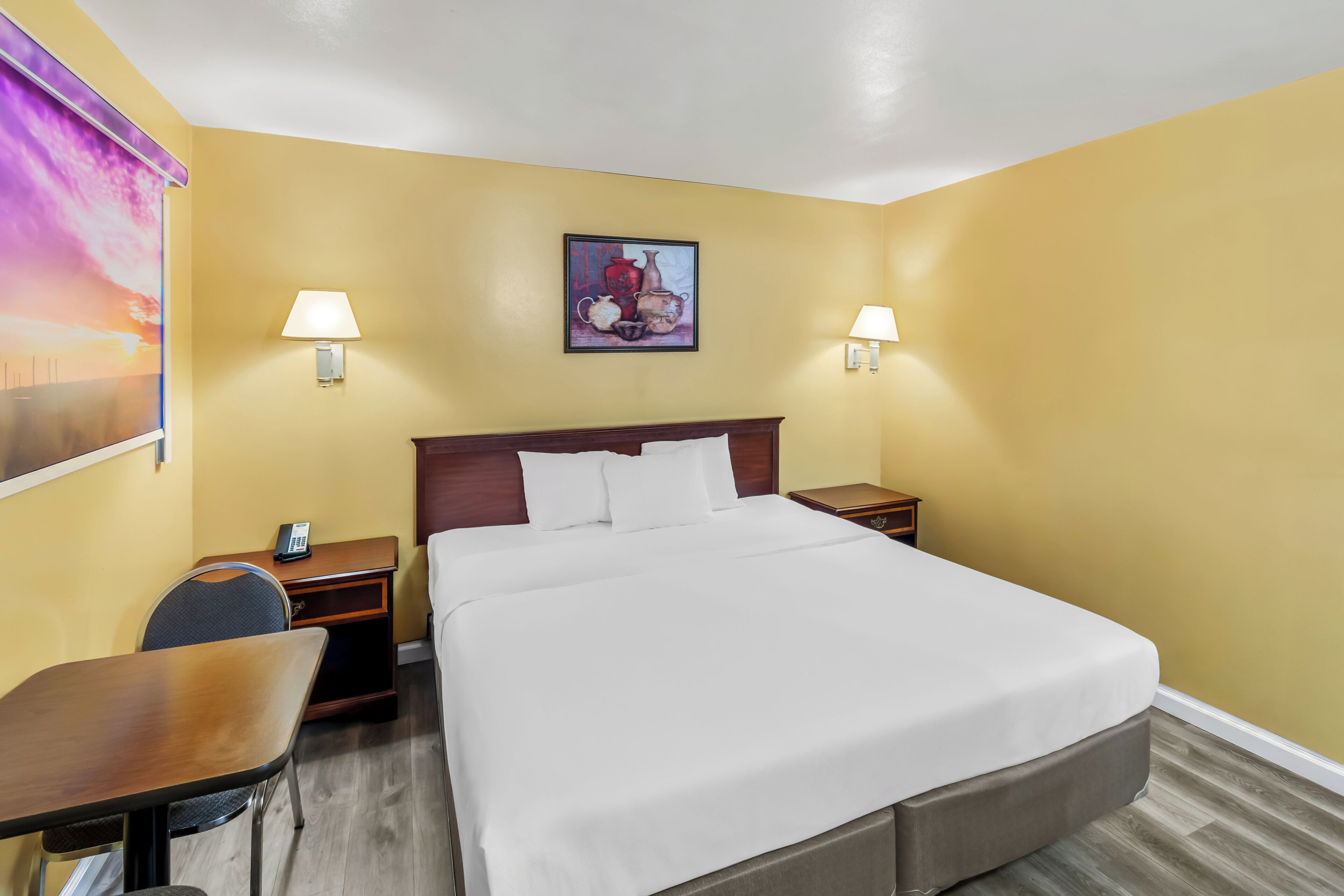 A hotel room with a large bed, two bedside lamps, a desk, and a chair.